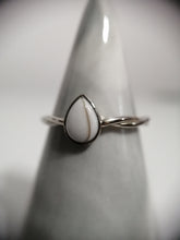 Charger l'image dans la galerie, Un gros plan d'une Bague Twist en argent de MONA fine joaillerie avec une pierre précieuse en forme de larme blanche nacrée, exposée sur un support effilé avec un fond flou pour mettre en valeur le bijou.