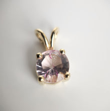 Charger l&#39;image dans la galerie, Vue rapprochée du Pendentif Solitaire Éternel de MONA fine joaillerie, doté d&#39;une pierre précieuse rose ronde facettée comme pierre centrale sertie dans une élégante monture à quatre griffes en or 10 carats. Le design est simple mais sophistiqué, avec une bélière dorée en haut pour l&#39;attacher à une chaîne. Le fond est une surface blanche et lisse.
