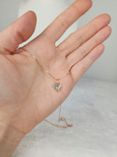 Charger l&#39;image dans la galerie, Une main tient le Pendentif Mini Coeur de MONA fine joaillerie, un délicat collier en chaîne d&#39;or avec un petit pendentif irisé en forme de cœur, doucement éclairé sur un fond neutre.
