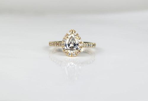 Une bague de fiançailles en diamant Bague Bonheur Éternel en forme de poire étincelante avec un serti halo et un anneau pavé, présentée sur un fond blanc épuré. Cette pièce est une création exquise de MONA fine joaillerie.