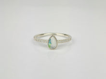 Charger l&#39;image dans la galerie, La (Copie) Bague Goutte de vie vers le haut de MONA fine joaillerie est une bague en argent ornée d&#39;une opale en forme de poire aux teintes vertes et bleues, rehaussée de zircon cubique, présentée sur un fond blanc uni.
