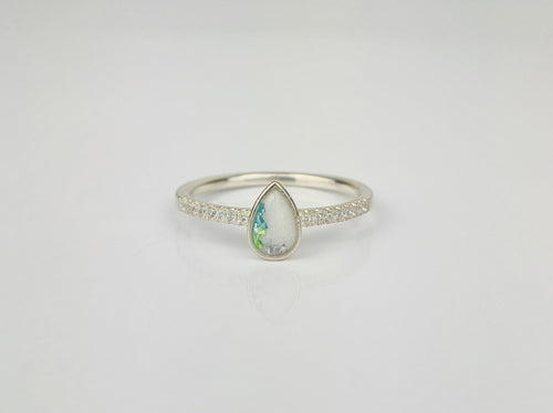 La (Copie) Bague Goutte de vie vers le haut de MONA fine joaillerie est une bague en argent ornée d'une opale en forme de poire aux teintes vertes et bleues, rehaussée de zircon cubique, présentée sur un fond blanc uni.