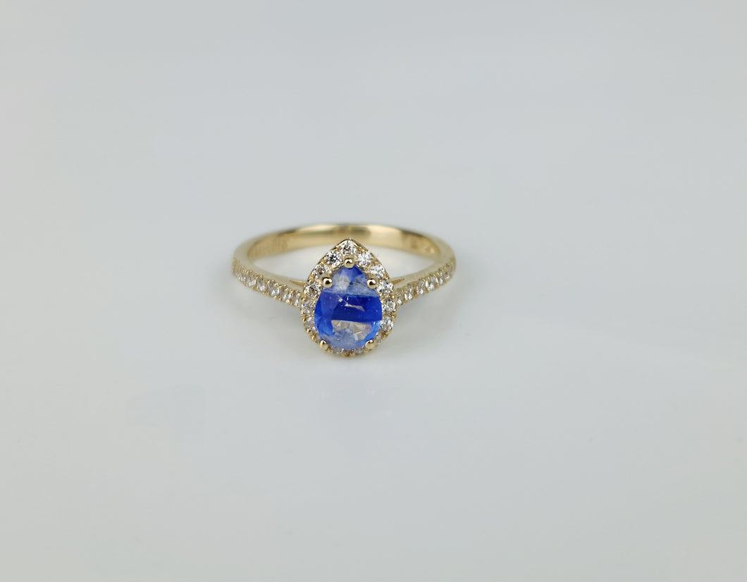 La Bague Bonheur Éternel de la Bijouterie Langlois est une bague en or 10 carats avec une superbe pierre centrale goutte bleue en son centre, entourée de petits diamants. L'anneau est également orné de minuscules diamants, rehaussant son éclat et son élégance. Présentée sur une surface blanche unie, cette pièce est vraiment exquise.