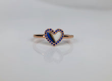 Charger l&#39;image dans la galerie, La Bague Coeur avec zircons de MONA fine joaillerie présente un design minimaliste en or avec une pièce centrale en forme de cœur soulignée de pierres bleues, partiellement ouverte au centre, sertie sur un fond blanc avec son reflet visible en dessous.
