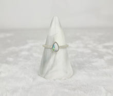 Charger l&#39;image dans la galerie, La Bague Goutte de vie vers le haut (avec zircons) de MONA fine joaillerie, ornée d&#39;une opale en forme de goutte et de zircons étincelants, est élégamment mise en valeur sur un cône de marbre blanc avec un fond blanc doux.
