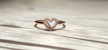 Charger l&#39;image dans la galerie, La Bague Coeur avec zircons de MONA fine joaillerie présente une pierre blanche en forme de cœur entourée de zircons étincelants, présentée sur une surface en bois clair.
