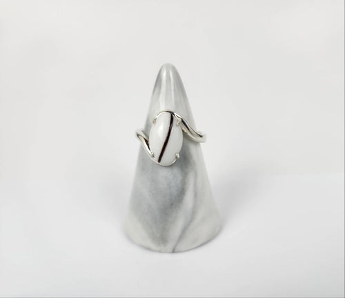 Une bague Bague Cynthia élégante et moderne au design minimaliste, comportant une inclusion de lait maternel, présentée sur un support en forme de cône sur fond blanc par MONA fine joaillerie.