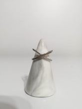Load image into Gallery viewer, Un cône porte-bague blanc simpliste présentant une paire de Bague Crossover croisée de MONA fine joaillerie avec des zircons étincelants de couleur diamant, sur un fond blanc épuré.
