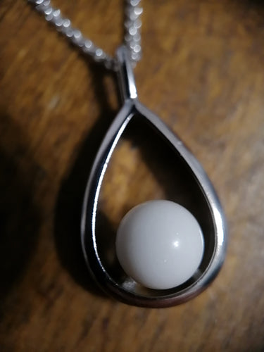 Élégant pendentif en argent avec une perle blanche ronde nichée dans une monture en forme de larme, mise en valeur sur une surface en bois par Bijoux La Précieuse.