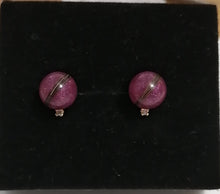 Load image into Gallery viewer, Une paire de Boucles d&#39;oreilles Juri sphériques violettes avec un détail de rayures argentées sur fond noir.
