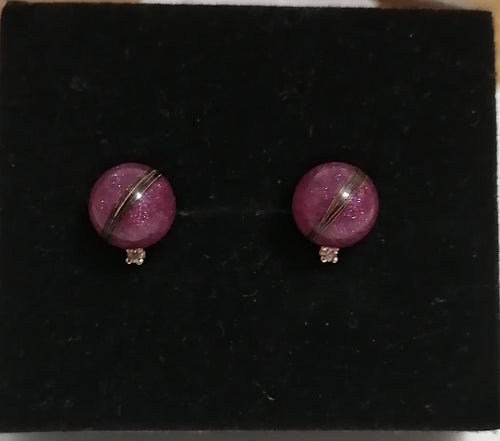 Une paire de Boucles d'oreilles Juri sphériques violettes avec un détail de rayures argentées sur fond noir.