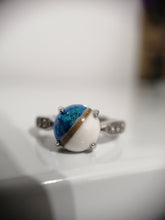 Load image into Gallery viewer, Une vue rapprochée d&#39;une Bague modèle 3 au design complexe avec une demi-perle bleue et blanche, rappelant une planète miniature, nichée entre les détails d&#39;un bracelet en argent de Bijoux La Précieuse.
