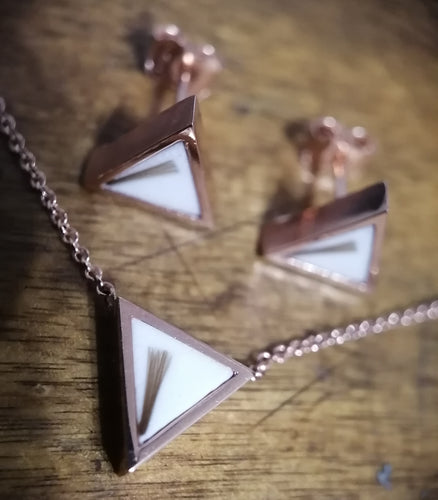 Un ensemble de bijoux triangulaires géométriques de MONA joaillerie fine, avec une finition en or rose et des incrustations blanches, comprenant des boucles d'oreilles et un collier Triangle disposés sur une surface en bois, mettant en valeur leur.