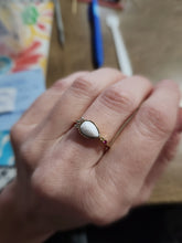 Load image into Gallery viewer, Une élégante bague ovale avec une pierre blanche sertie dans un anneau d&#39;or, mise en valeur sur la paume d&#39;une personne par MONA fine joaillerie.
