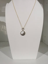 Charger l&#39;image dans la galerie, Un élégant collier pendentif Cabella exposé, présentant un design circulaire avec une pierre précieuse centrale, présenté sur une forme de buste blanc par MONA fine joaillerie.
